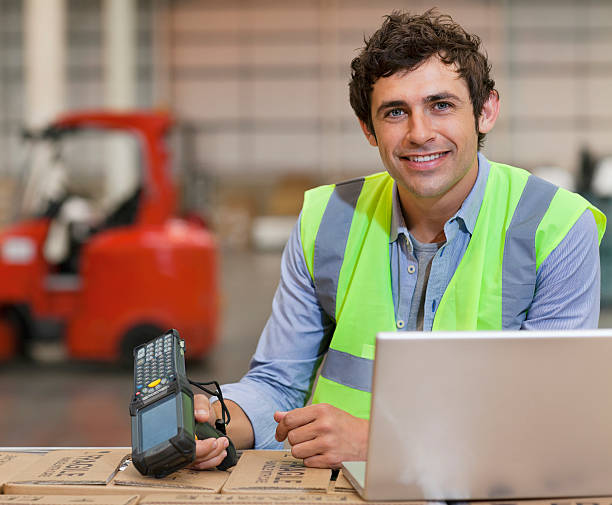 sorridente jovem trabalhador de armazém com leitor de código de barras e computador portátil - bar code reader wireless technology computer equipment imagens e fotografias de stock