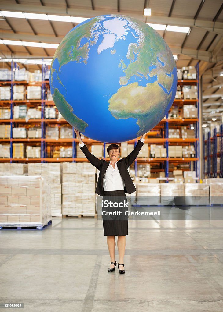 Mature woman holding aloft a large blue ball in warehouse  Globe - Navigational Equipment Stock Photo