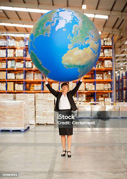 Mature Woman Holding Aloft A Large Blue Ball In Warehouse Stock Photo - Download Image Now