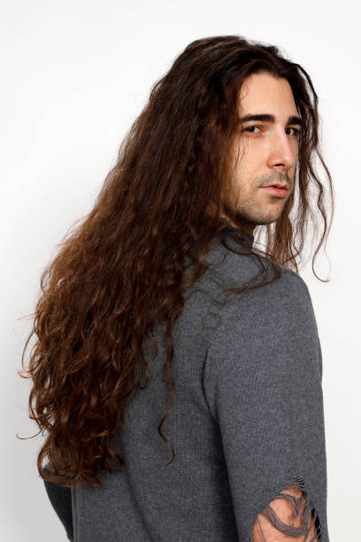 istock Attractive young guy with very long curly hair is posing in studio. 1319825081