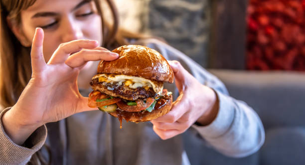 istock Big appetizing burger with meat in female hands in a cafe. 1319828903