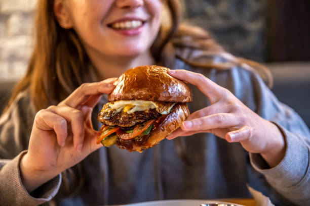 istock Big appetizing burger with meat in female hands in a cafe. 1319828908