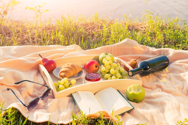 istock Picnic by the river. On a light-colored bedspread, a wooden tray with fruit, cakes and a bottle of wine. 1319829549