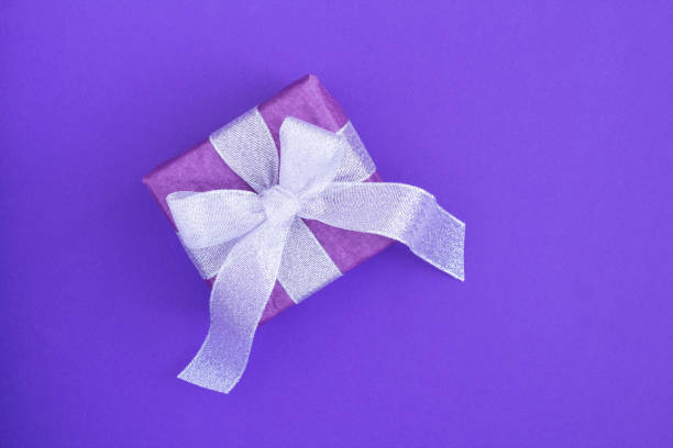 istock Top view of gift box with silver bow on the purple background 1319831176