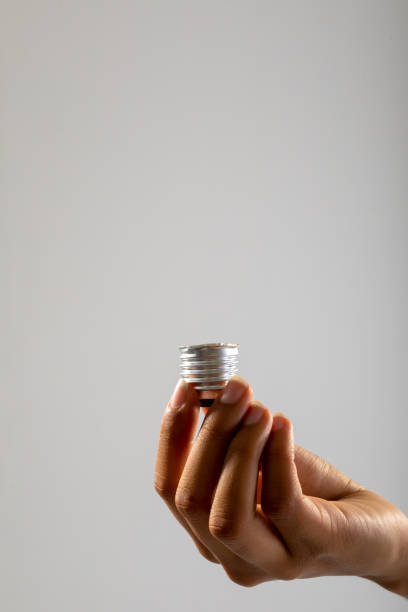 istock Close up of hand holding bulb screw base against grey background 1319834014