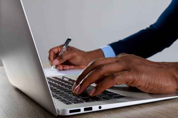 istock Close up of businessman using laptop and taking notes against grey background 1319835219