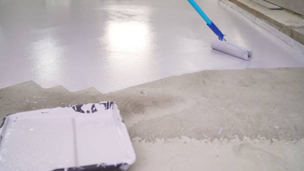 A worker paints the floor with white paint using a roller. . Application of paint with a paint roller. use a paint roller when working indoors and treating the floor. un trabajador aplica pintura blanca con un rodillo. aplicación de pintura con rodillo de pintura. utilizar un rodillo de pintura cuando se trabaja en interiores y tratar el suelo. un trabajador pinta el suelo con pintura blanca con un rodillo.
