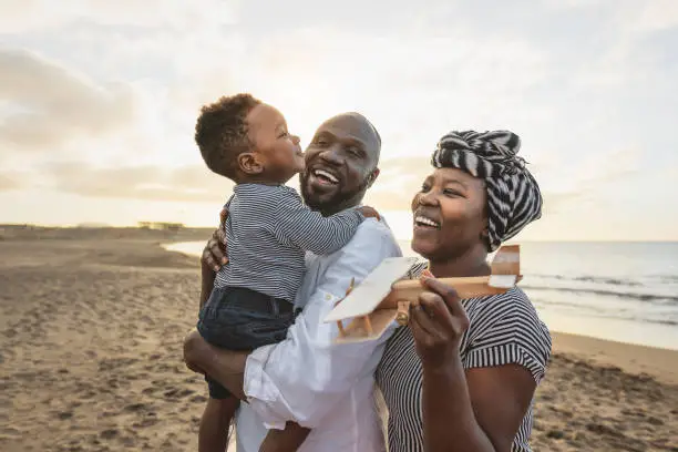 Photo of Happy African family having fun on the beach during summer vacation - Parents love and unity concept