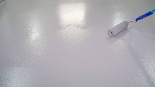 Man painting the floor. The floor is painted white with a roller. Blue paint roller, on white background stock photo