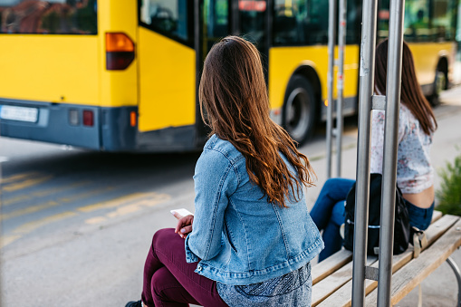 Young Caucasian women at a bus stop in social distancing waiting a bus.