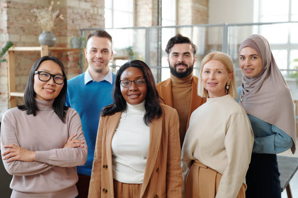 Interracial colleagues of modern company Group of smiling young interracial colleagues of modern company standing together in loft open space office organized group photos stock pictures, royalty-free photos & images
