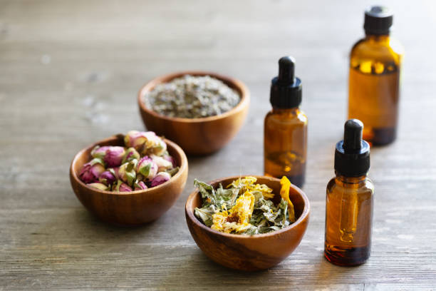 Dried herbs in wooden bowls and pipette bottle:  aromatherapy concept stock photo