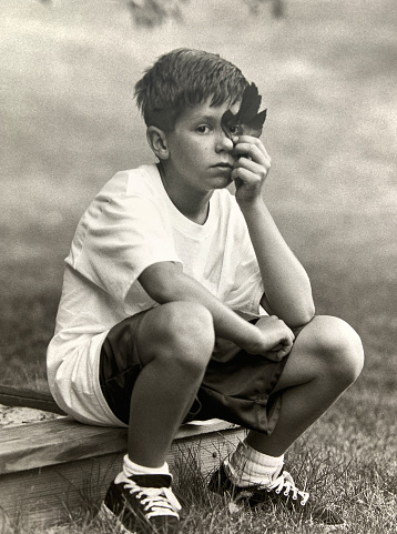 Young boy sitting and looking through leaf looking bored.