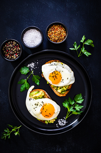 Continental breakfast - sunny side up eggs on toasted bread with avocado on black background