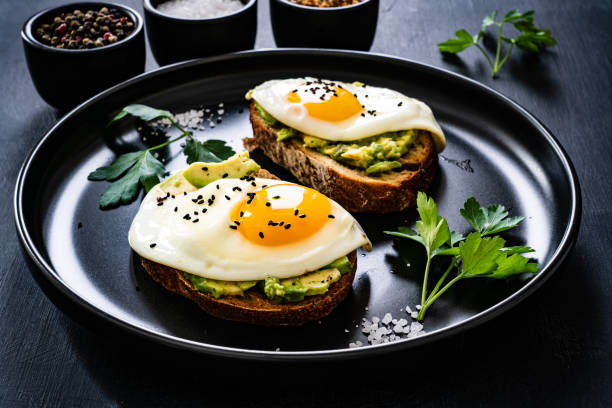 istock Continental breakfast - sunny side up eggs on toasted bread with avocado on black background 1319848445