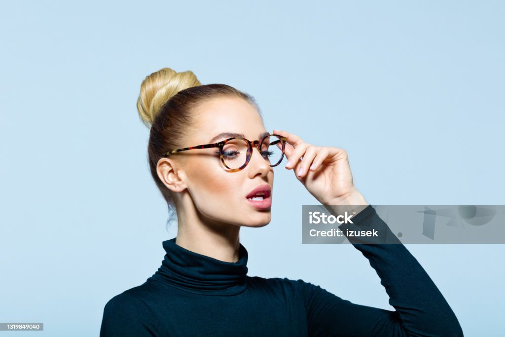 Headshot of confident elegant woman Confident woman wearing black turtleneck and eyeglasses looking away. Studio shot on blue background. Side View Stock Photo