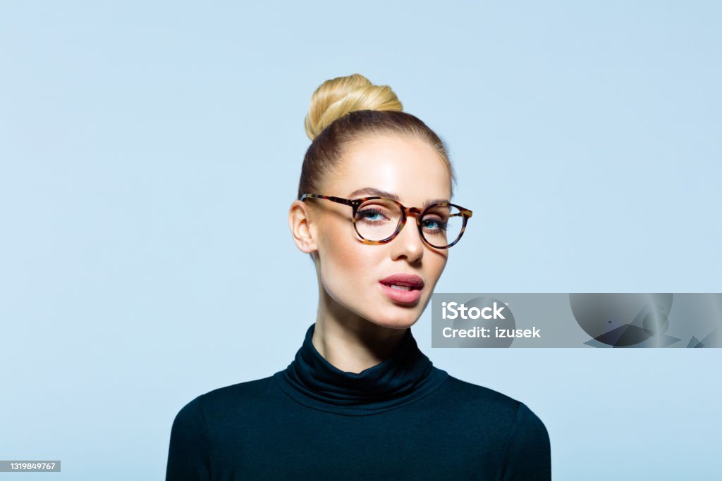 Headshot of confident elegant woman Confident woman wearing black turtleneck and eyeglasses looking at camera. Studio shot on blue background. Eyeglasses Stock Photo