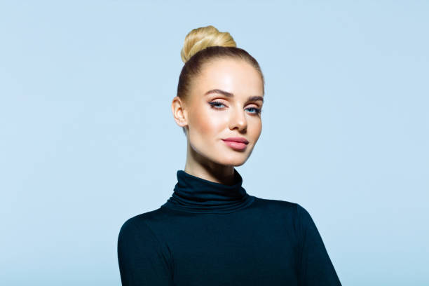 Headshot of confident elegant woman Confident woman wearing black turtleneck looking at camera. Studio shot on blue background. smirking stock pictures, royalty-free photos & images