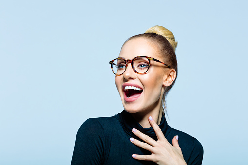 Happy woman wearing black turtleneck and eyeglasses looking away and laughing. Studio shot on blue background.