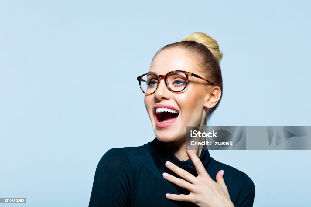 Headshot of excited elegant woman Happy woman wearing black turtleneck and eyeglasses looking away and laughing. Studio shot on blue background. Eyeglasses Stock Photo