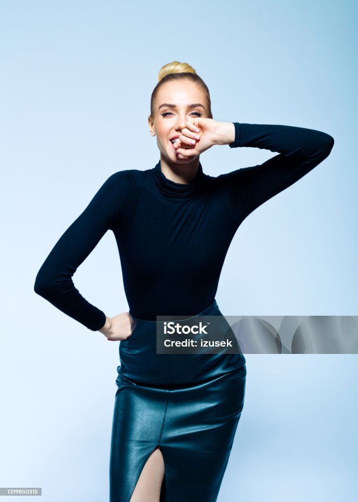 Portrait of cheerful elegant woman Happy woman wearing black turtleneck and skirt standing with hand on hip and smiling at camera. Studio shot on blue background. Laughing Stock Photo