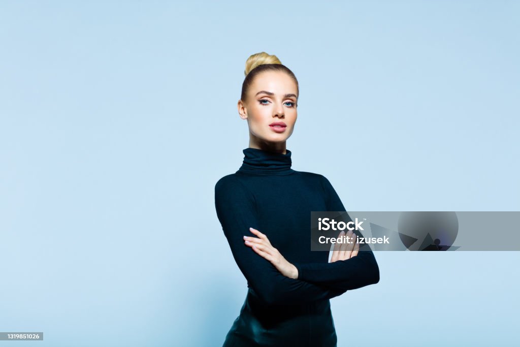 Portrait of confident elegant woman Confident woman wearing black turtleneck and skirt standing with arms crossed and looking at camera. Studio shot on blue background. Business Stock Photo
