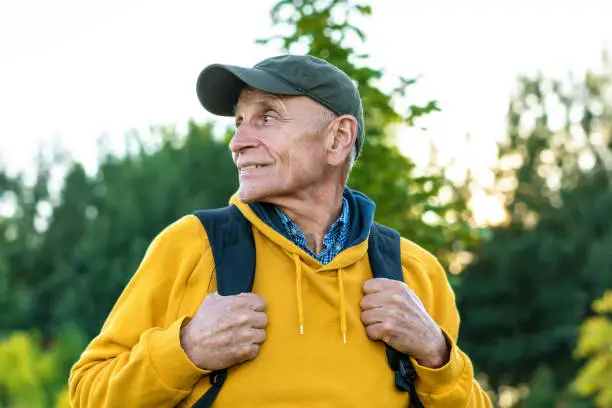 Aged happy traveler in cap and yellow hoodie looking aside in mountains. Concept connecting with nature.