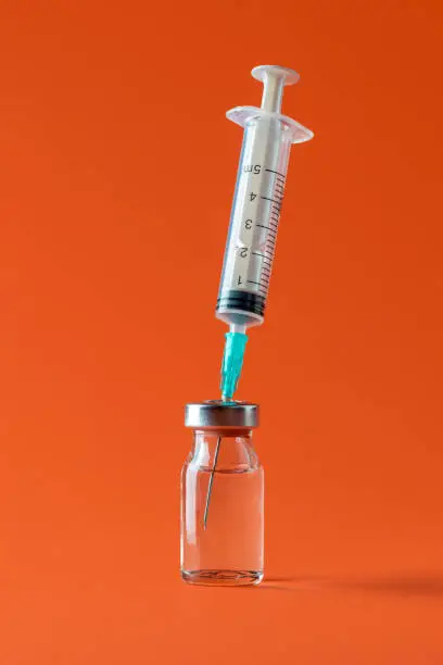 Bottle with medication drug and a syringe with needle minimalist on an orange background. Vaccine vial isolated on a colored background.