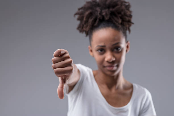 unimpressed young woman giving a thumbs down gesture - downgrade imagens e fotografias de stock