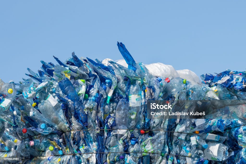 Used plastic trash. Pressed beverage packagings on a blue sky background Recyclable PET bottles with colored caps baled for garbage collection to processing plant. Waste sorting, recycling or disposal Plastic Pollution Stock Photo