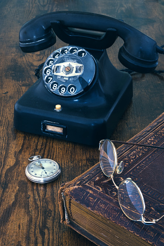 bodegón de teléfono viejo, reloj de bolsillo, libro y gafas en mesa de madera photo
