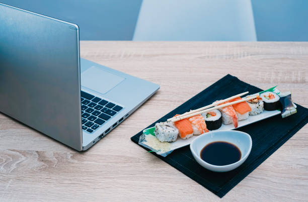 istock Work table on which there is a laptop computer and a plate with sushi on a black mat. 1319856982