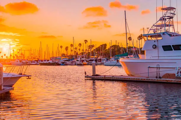 Oranges and pinks highlight all the boats, water and sky in Oceanside Harbor, near Carlsbad, California in Southern California.