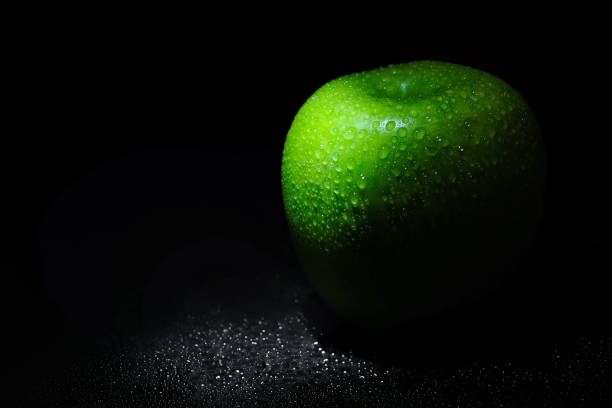 Ripe green apple with water drops on a black background.