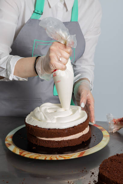 istock Woman hands chef spreading cream on second layer of Chocolate cake. Making Chocolate Layer Cake. Series. 1319866031