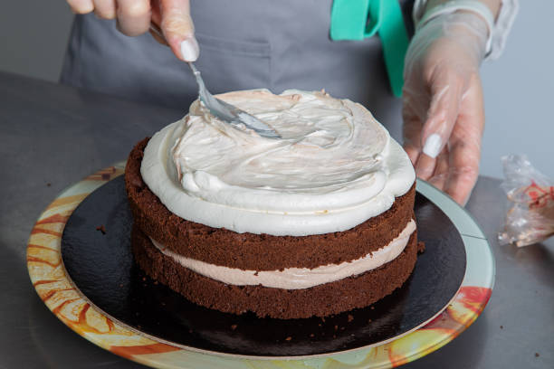 istock Woman hands chef spreading cream on second layer of Chocolate cake. Making Chocolate Layer Cake. Series. 1319866033