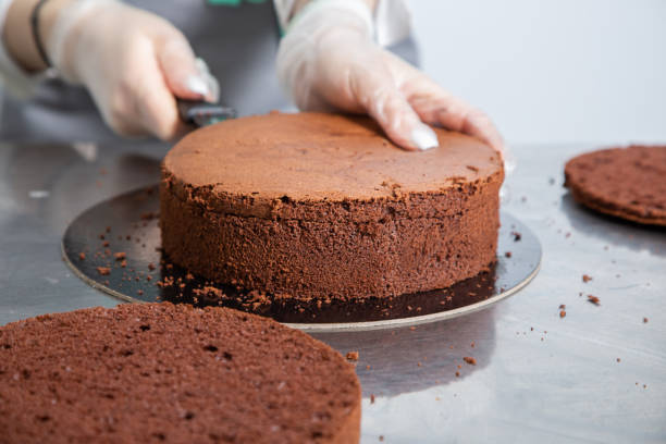 istock Womans hands chef cutting chocolate cake layers and stacking them on metal table. Making Chocolate Layer Cake. Series. 1319866034