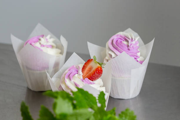 istock Cupcakes decorated with butter cream in white baking parchment cases on metal table in a professional confectionery studio. 1319866041