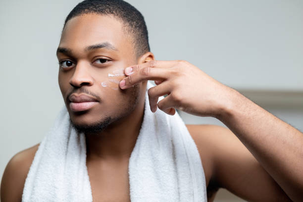 hombre africano cuidado de la piel masculino aplicando crema facial - male towel men human face fotografías e imágenes de stock