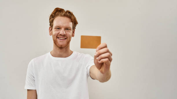 młody rudy mężczyzna trzyma kartę kredytową przed nim - men suit holding human finger zdjęcia i obrazy z banku zdjęć