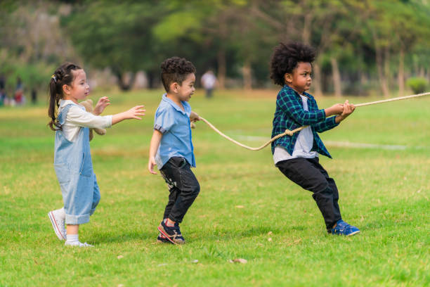 istock diverse mixed race kids boy and girl having fun playing pulling rope together in park during summer 1319886396