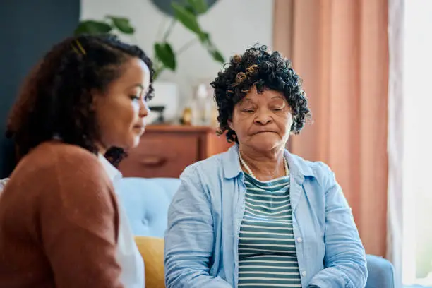 Photo of Shot of an elderly woman sitting with her daughter on the sofa at home and not talking