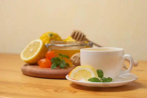 Ginger tea with mint and lemon. Healthy and hot drink. Liquid honey in honey-jar. White cup on wooden background. Selective focus. High quality photo