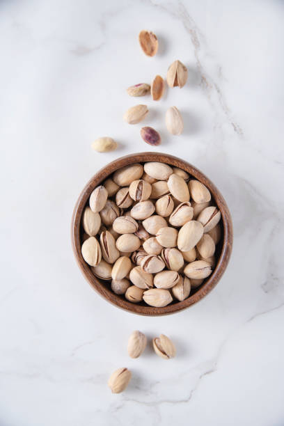 istock Pistachio nuts in a brown bowl on a white marble background. Top view and copy space 1319902404