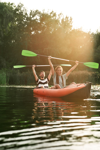 Couple of excited friends having fun while kayaking in a river surrounded by the beautiful nature on a summer day. Kayaking, travel, leisure concept