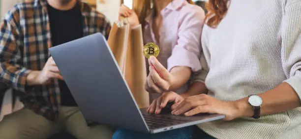 Group of young people using laptop and bitcoin for shopping online together