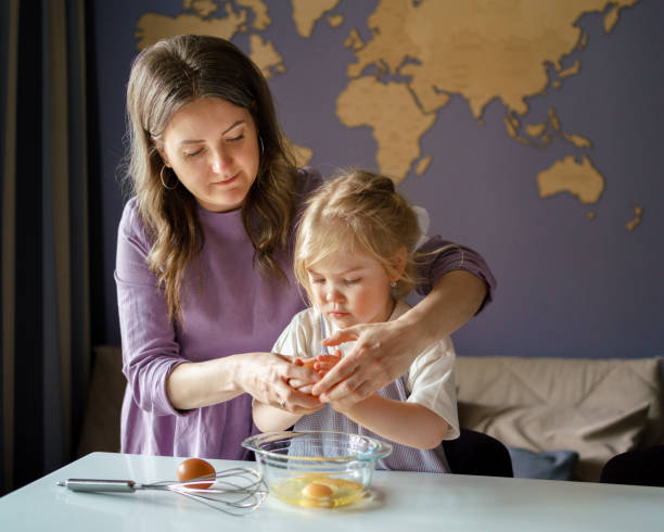 maman apprend au petit enfant à cuisiner tout en passant du temps à la maison - break eggs domestic kitchen breaking photos et images de collection