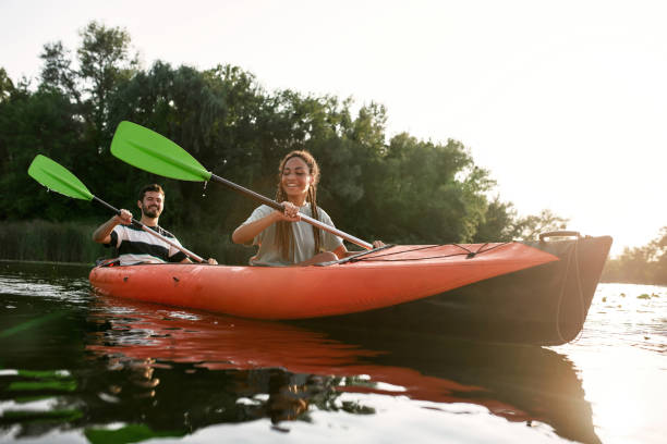 sorridente giovane donna e il suo ragazzo che si godono il kayak in un lago nel tardo pomeriggio estivo - men sitting canoe canoeing foto e immagini stock