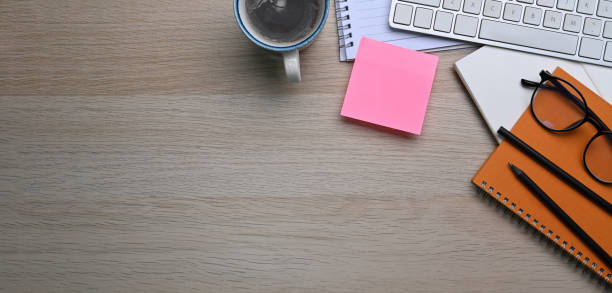 Above view office desk with sticky note, coffee cup, keyboard and notebook on wooden table.