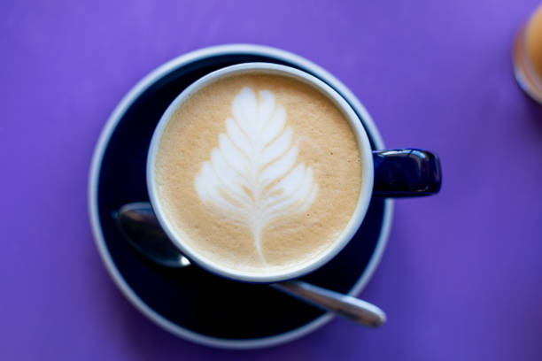 istock Cup of latte coffee with a drawn leaf on a purple table, horizontal 1319914192